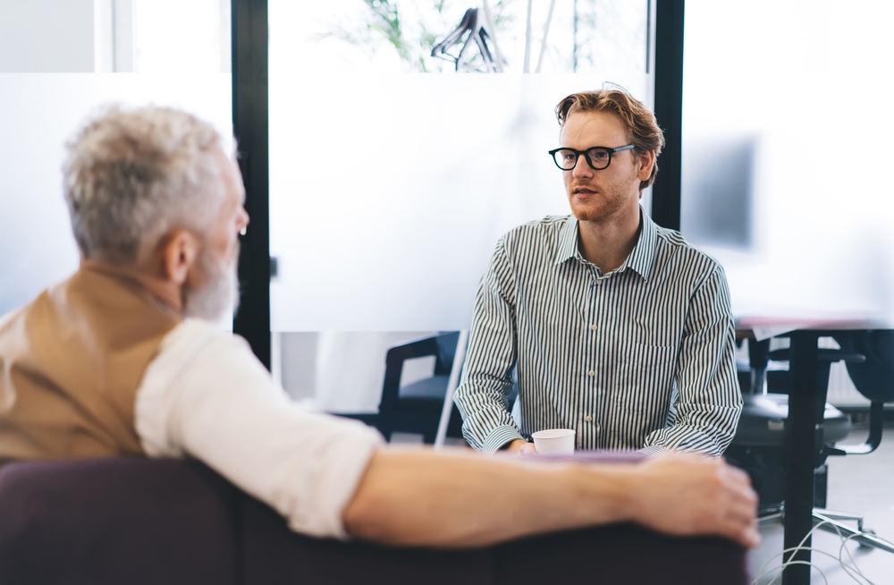 Young,Businessman,Attentively,Listens,To,Senior,Mentor,During,Private,Office